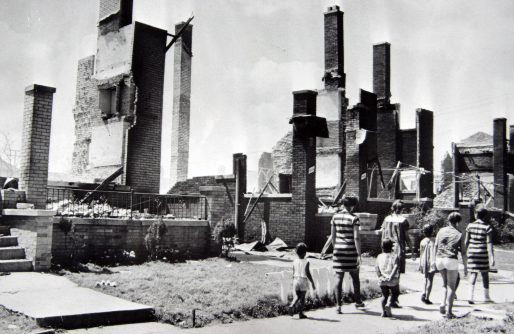 In this July 25, 1967, file photo, women and children stroll past the burned remains of homes after riots in Detroit on July 23. The houses were a short distance from 12th Street, center of the riot activity. (AP)