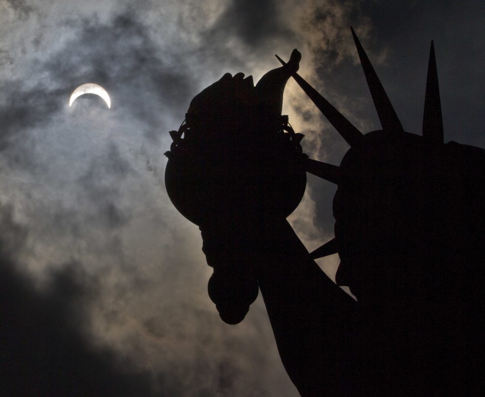 The partial solar eclipse appears over the Statue of Liberty. (Seth Wenig/AP)