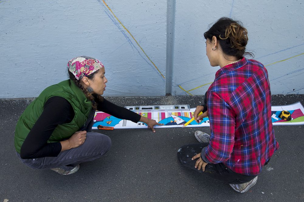 Artist Silvia López Chavez points out a detail of her mural design to a volunteer, artist Silvi Naçi. (Jesse Costa/WBUR)