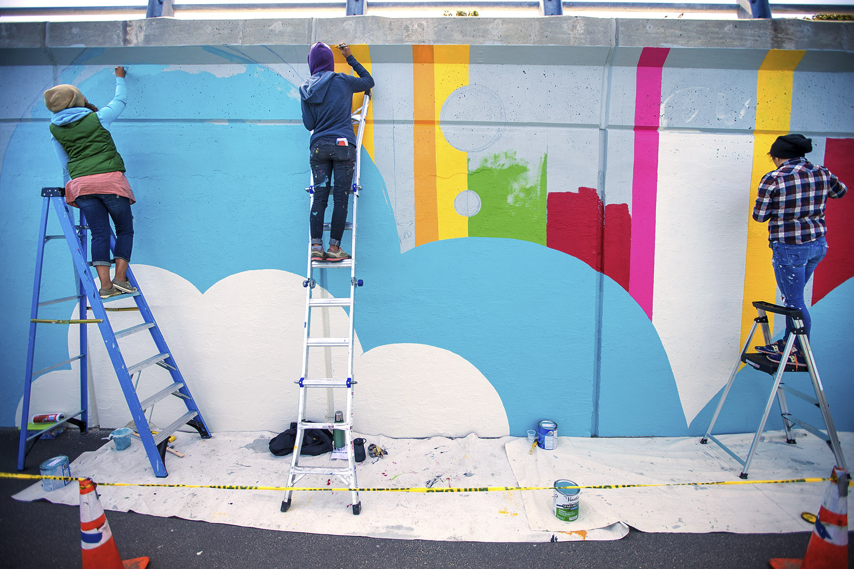 From left, artists Silvia López Sanchez, Sara Barrientos and Laura Mennucci work on the main section of the mural as it takes shape. (Jesse Costa/WBUR)