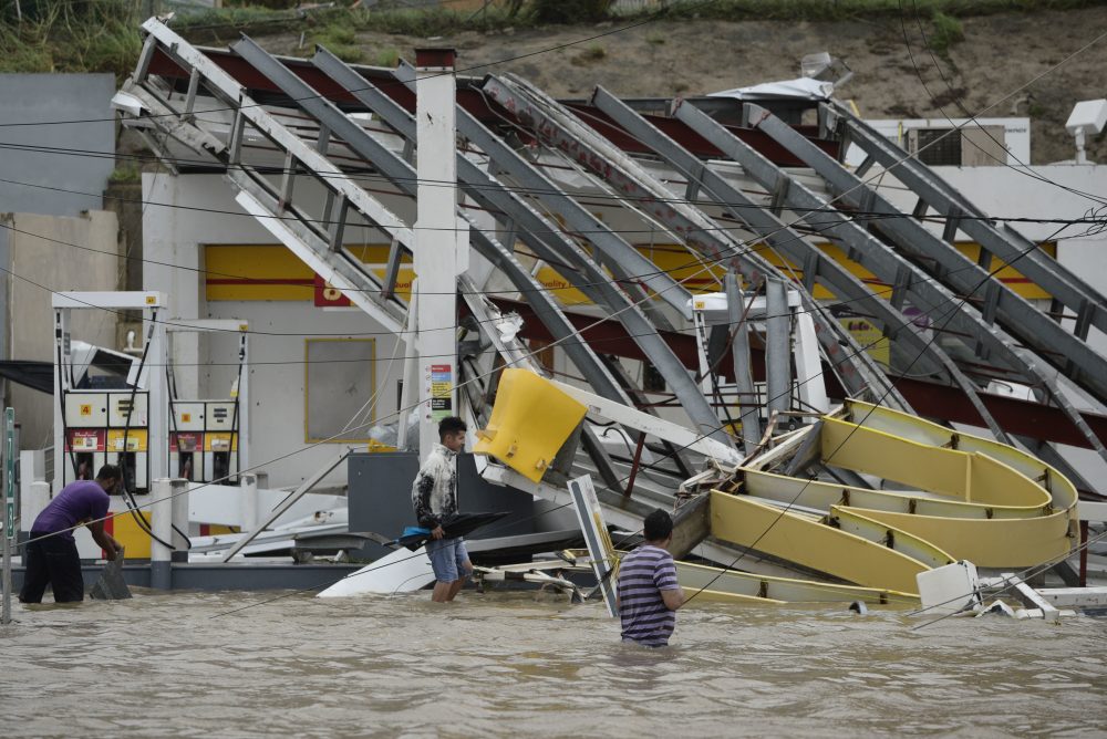 People walk next to a gas station flooded and damaged by the impact of Hurricane Maria in Humacao, Puerto Rico on Wednesday. (Carlos Giusti/AP)