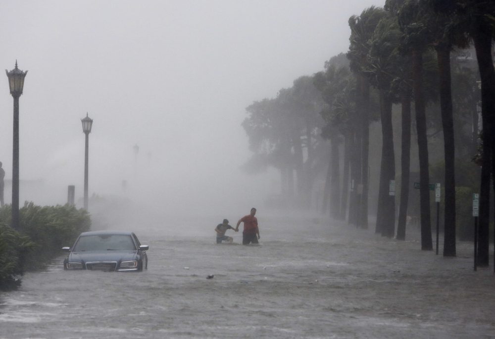 This Sept. 11, 2017 file photo shows pedestrians walking by on a flooded street as Tropical Storm Irma hits Charleston, S.C. While preliminary data suggest Irma's eye pushed a surge of more than 10 feet hit onto southwest Florida's Marco Island, the highest water levels were reported hundreds of miles away in Jacksonville, Fla., and Savannah, Ga., according to the National Oceanic and Atmospheric Administration. (Mic Smith/AP)