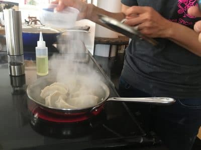 Adding water to the skillet in order to steam the dumplings. (Meghna Chakrabarti/WBUR)