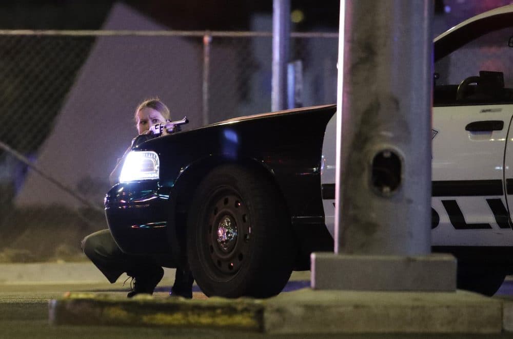 A police officer takes cover behind a police vehicle Sunday night. (John Locher/AP)