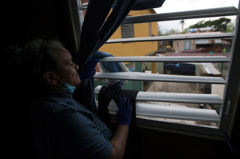 Rosa Serrano looks out the window at other homes that have been damaged by Maria in the Juana Matos Community of Cataño. (Jesse Costa/WBUR)