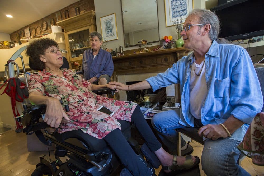 Ron Hoffman, right, visits the Boston home of Susan Kron, who has ALS, and her husband Paul Schaffrath. (Jesse Costa/WBUR)