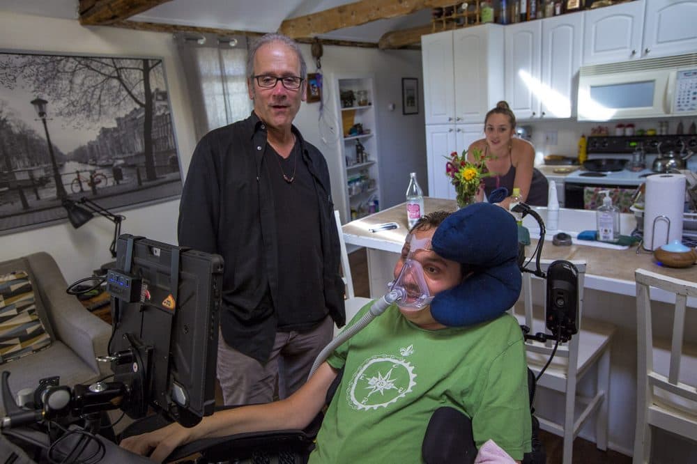 In this 2016 photo, Bobby Forster communicates with Hoffman with a computer that uses an eye-tracking device mounted onto his wheelchair. Forster's wife, Casey, is behind. Casey Forster and Hoffman had just discussed the prospect of a road trip to New Orleans. (Jesse Costa/WBUR)
