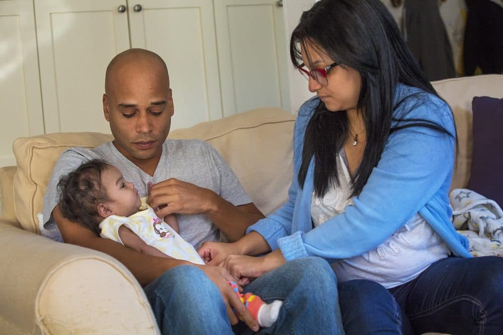 Andino hands Amaia, to father Kelvin Garcia to hold while she fixes Amaia's jumper. (Jesse Costa/WBUR)