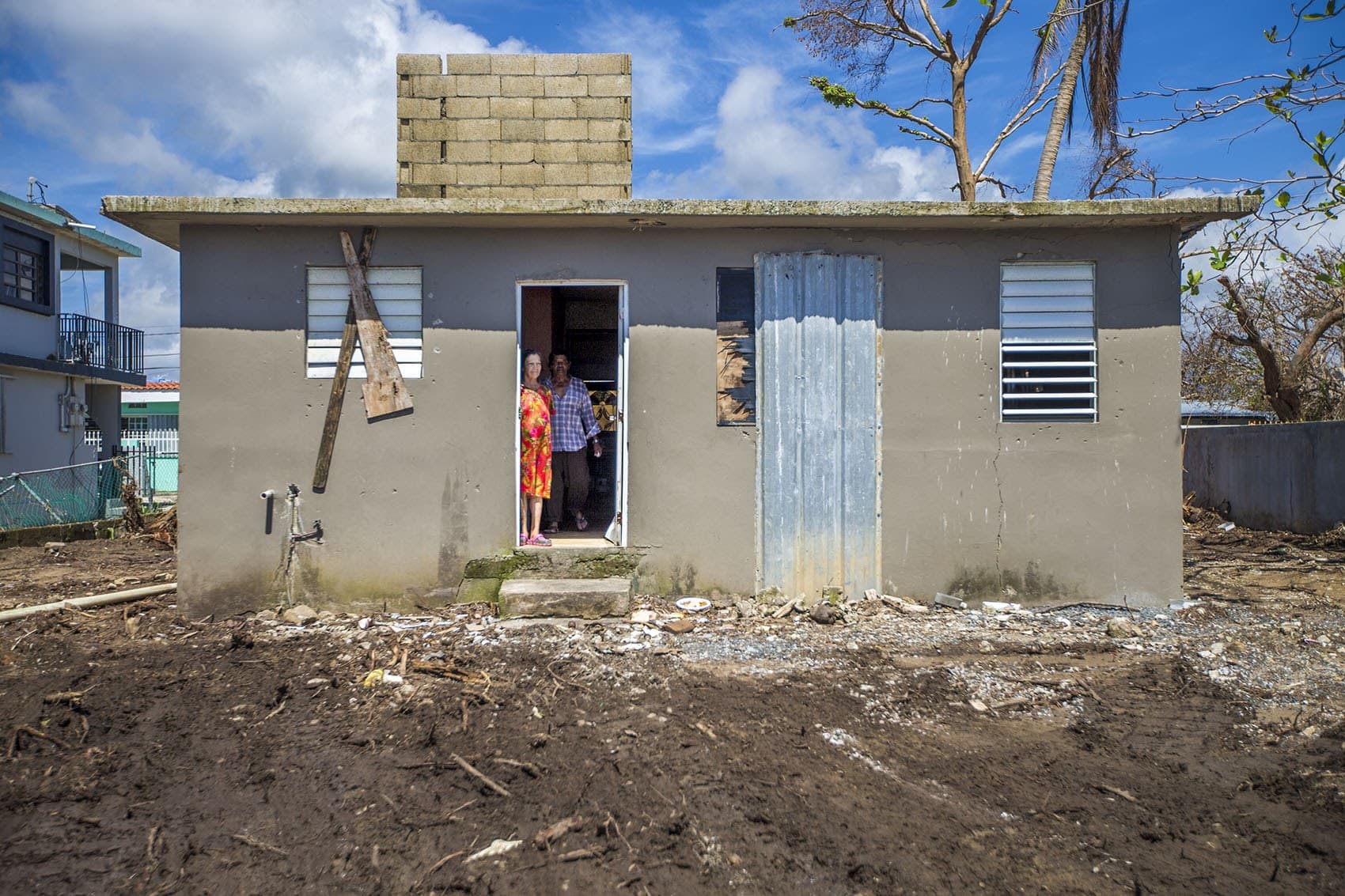 A man and a woman look outside their beaten and weathered house in Punto Santiago where Hurricane Maria first made landfall. (Jesse Costa/WBUR)