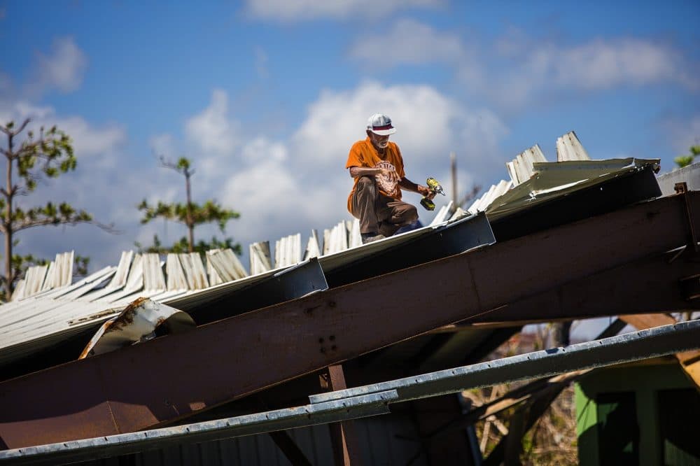 A worker removing the bolts of a roof of a metal structure that had collapsed during Hurricane Maria. (Jesse Costa/WBUR)