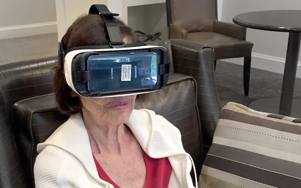 Janice Bornstein, 83, wears a virtual reality headset. The device puts her in front of her childhood home in Syracuse. (Rachel Zimmerman/WBUR)
