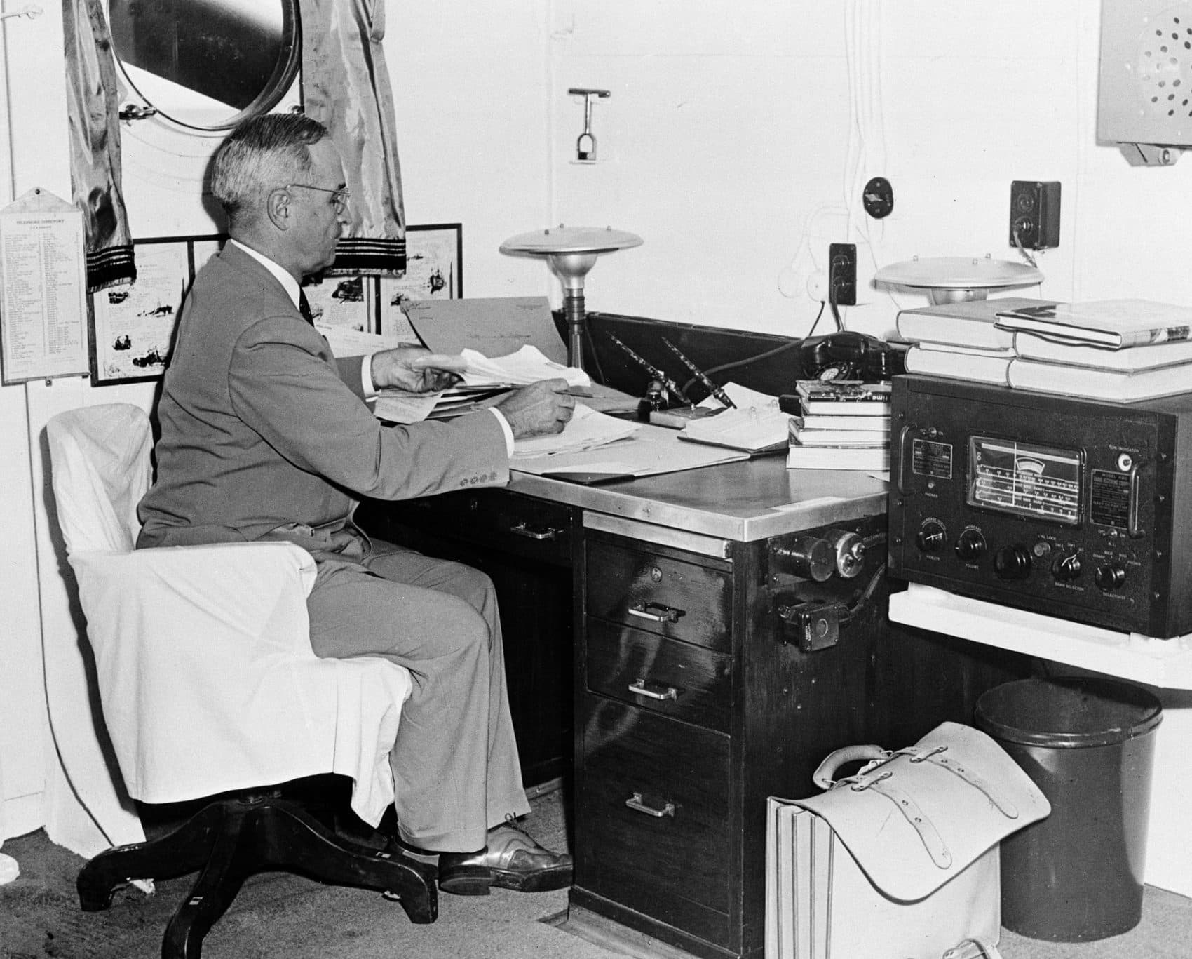 Aboard the cruiser Augusta, President Harry S. Truman, with a radio at hand, reads reports of the first atomic bomb raid on Japan, Aug. 6, 1945, while en route home from the Potsdam conference, where the Japanese flatly rejected the Potsdam Declaration. (AP Photo)