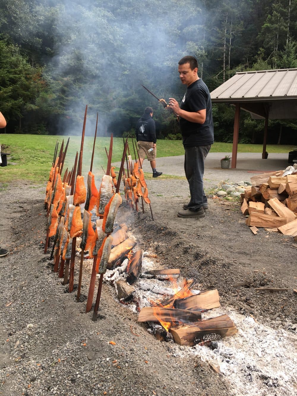 At the 55th Annual Yurok Salmon Festival, Oscar Gensaw cooks salmon the traditional way, on redwood skewers around a fire pit. This year, though, the tribe had to purchase salmon from Alaska. (Lisa Morehouse/KQED)