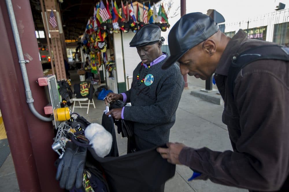 Babacar Thiam, left, of Good Mother Clothing and Jewelry in the Dudley Square MBTA station, assists Mike White. (Jesse Costa/WBUR)