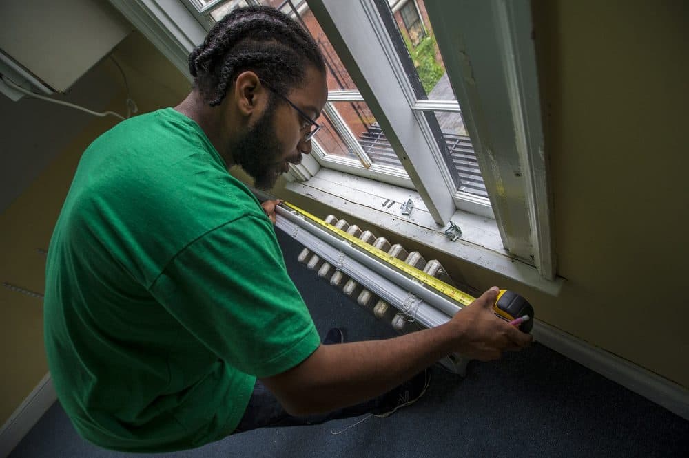 Ennis measures a window shade during the job at the Tellus Institute in Cambridge. (Jesse Costa/WBUR)