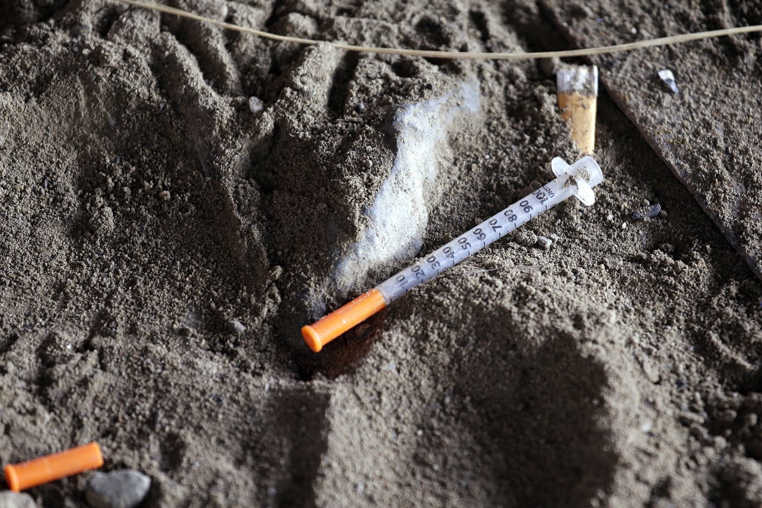 A discarded syringe sits in the dirt with other debris under a highway overpass in Washington state. (Elaine Thompson/AP)