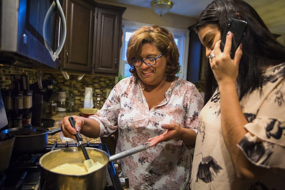 As Irma Flores stirs mik in a pan, her daughter Gabriela Portillo-Perez speaks with her grandmother Isabel on the phone in El Salvador. (Jesse Costa/WBUR)