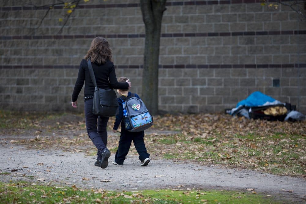 Caroline Toth-Bernstein walks with her 6-year-old son Oscar past a broken down tent and suitcase in a vacant lot they walk through every day to go to and from the Orchard Gardens K-8 Pilot School. (Jesse Costa/WBUR)