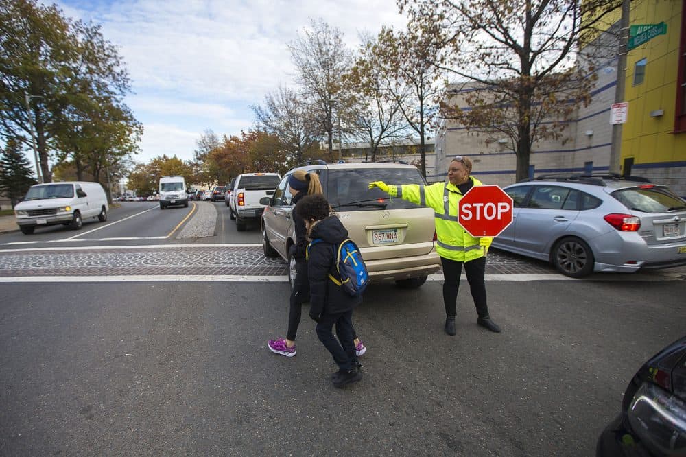 Crossing guard Karen Perry ushers an Orchard Gardens parent and her child across Melnea Cass Boulevard through busy traffic. (Jesse Costa/WBUR)