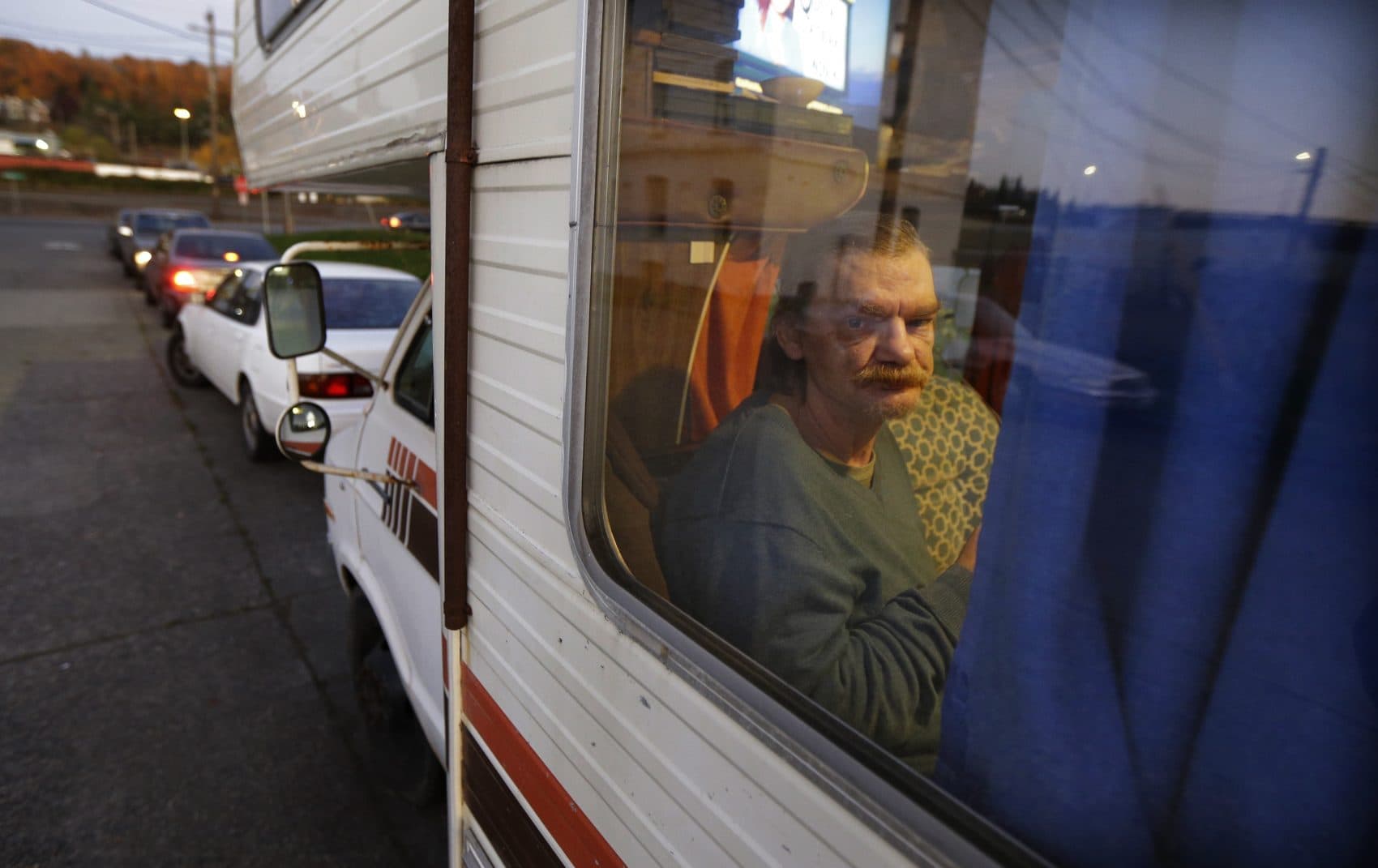 In this Oct. 30, 2017 photo, Stanley Timmings looks out of the window of the RV where he lives with his girlfriend on the streets of Seattle. Earlier in the year, the couple lost the room they were renting in a house when the owner died of cancer, and they were unable to find another room or an apartment that they could afford, so they bought the RV for $300. In Seattle, about one-third of unsheltered homeless people live in vehicles, according to recent homeless counts. (Ted S. Warren/AP)