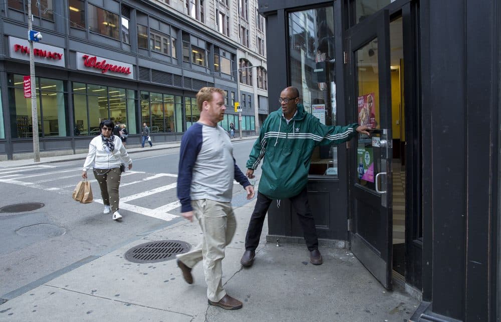 Higginbottom opens a door for someone while panhandling outside a Dunkin' Donuts in downtown Boston. (Robin Lubbock/WBUR)