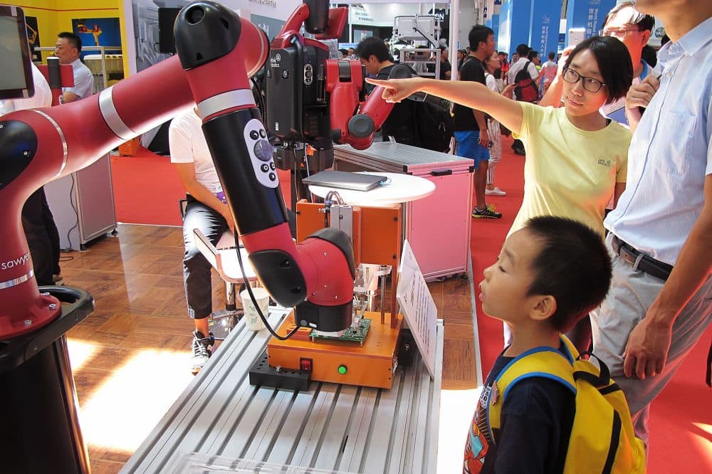 A young boy looks intently at a Rethink robot picking up a circuit board at the World Robot Conference in Beijing. (Asma Khalid/WBUR)