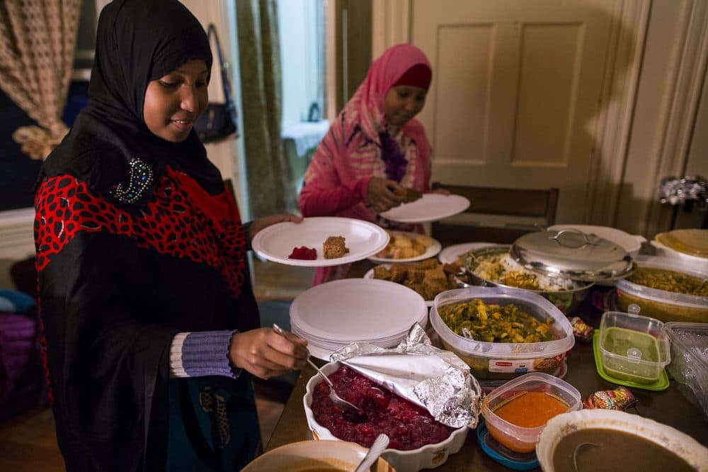 Hawo Ahmed helps herself to cranberry sauce as twin sister Muna picks up a piece of gingerbread during a Thanksgiving feast celebrated on Sunday with volunteers from the International Institute of New England. (Jesse Costa/WBUR)