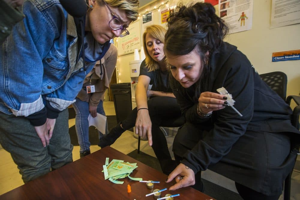 Needle exchange worker Emily Moulton, left, and Tapestry Health Director of HIV Health and Prevention Liz Whynott lean in to determine each test strip's result. All were postive for fentanyl. (Jesse Costa/WBUR)