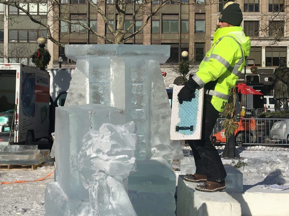 Ice sculptor Austin Lundbohm catches his balance as he prepares to sand down an ice platform in Copley Square. (Simon Rios/WBUR)