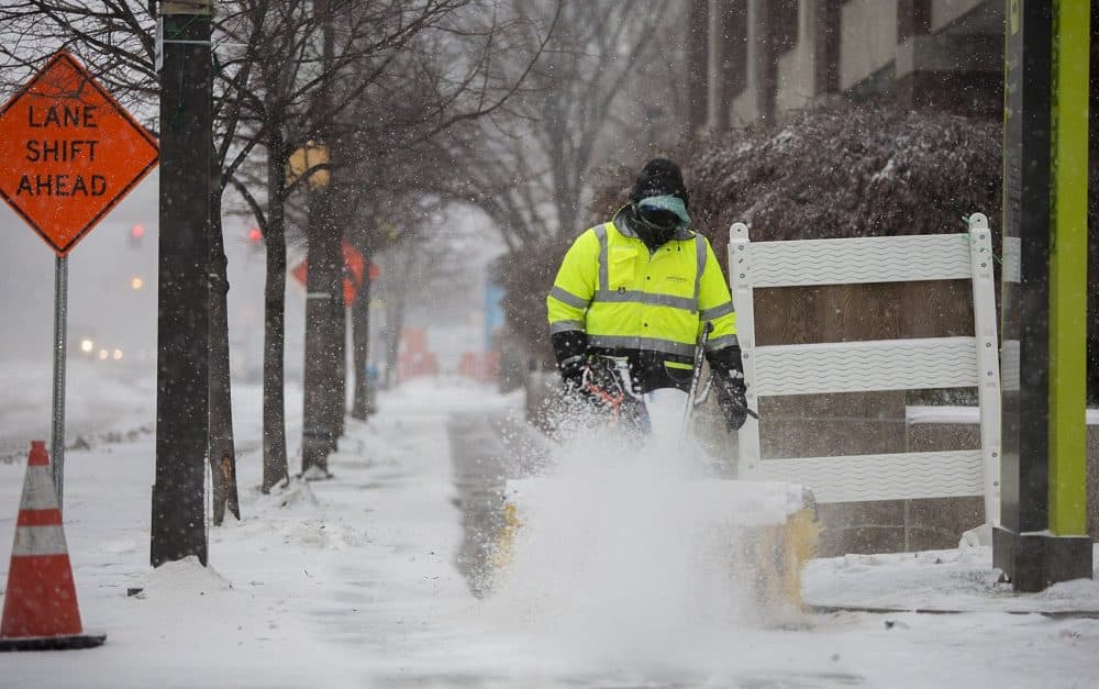 A man sweeping snow off the sidewalk on Broadway in Kendall Square. (Jesse Costa/WBUR)