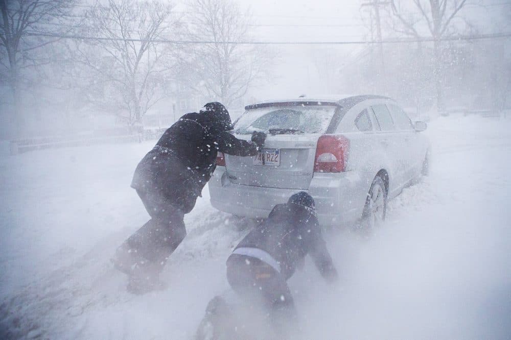 In white-out conditions, two men push a car stuck in the deep snow in Rockport. (Jesse Costa/WBUR)