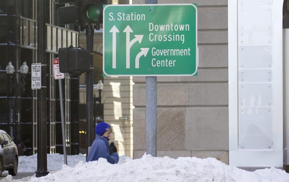 Half hidden by a snow bank, a woman walks through downtown Boston. (Robin Lubbock/WBUR)