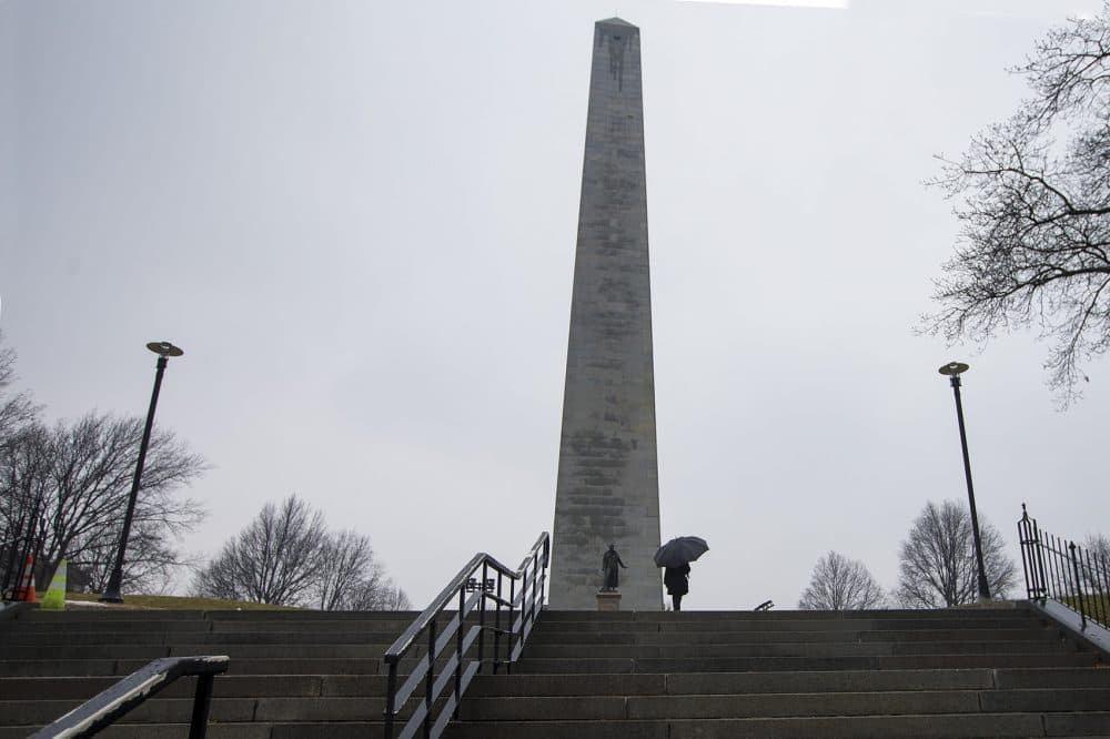 On a rainy Monday, a woman carrying an umbrella walks toward the Bunker Hill Monument, which has been closed due to the federal government shutdown. (Jesse Costa/WBUR)