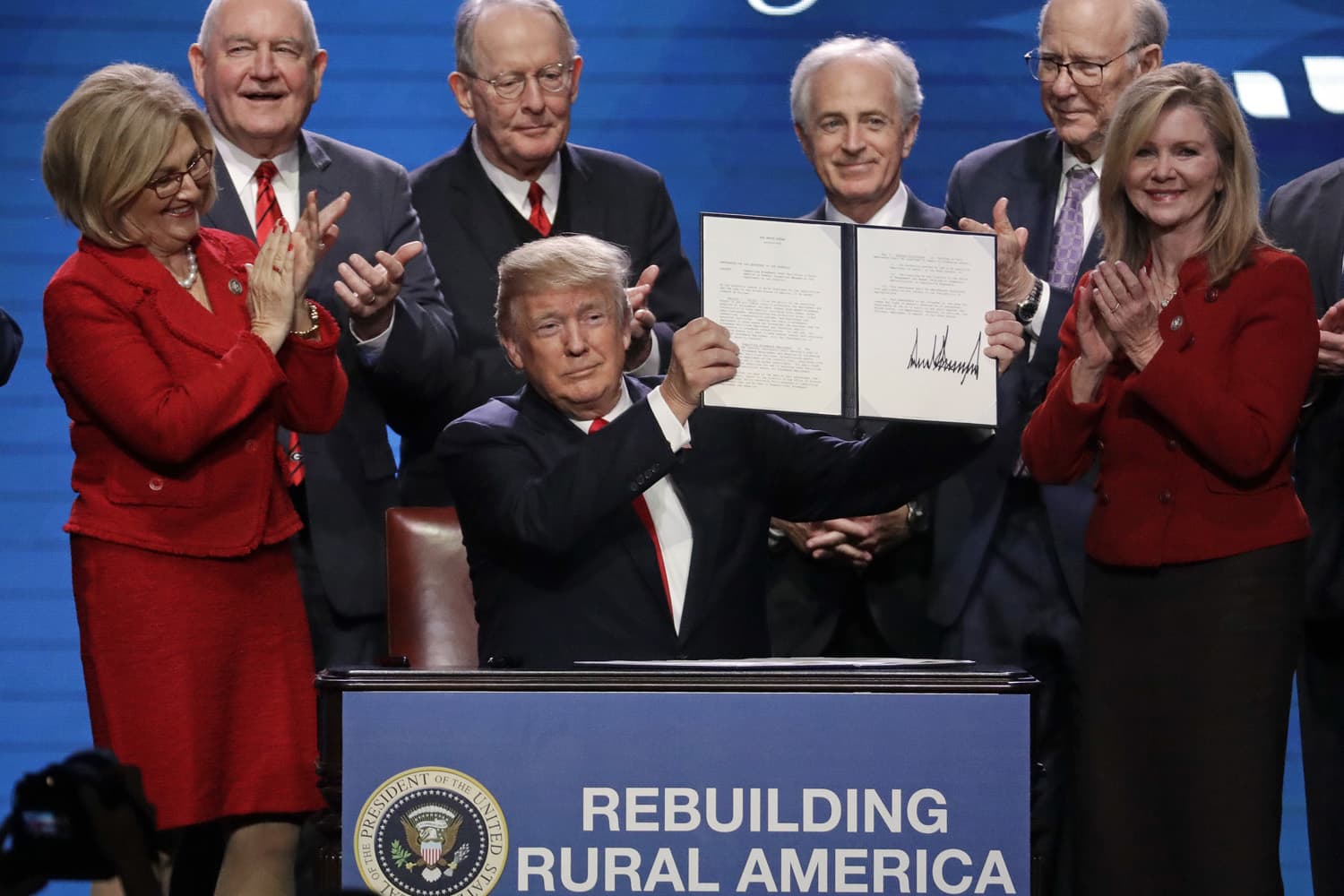 President Donald Trump holds up an executive order after signing it at the American Farm Bureau Federation annual convention Monday, Jan. 8, 2018, in Nashville, Tenn., as, from left, Rep. Diane Black, R-Tenn., Agriculture Secretary Sonny Perdue, Sen. Lamar Alexander, R-Tenn., Sen. Bob Corker, R-Tenn., Sen. Pat Roberts, R-Kan., and Rep. Marsha Blackburn, R-Tenn., applaud (AP Photo/Mark Humphrey)