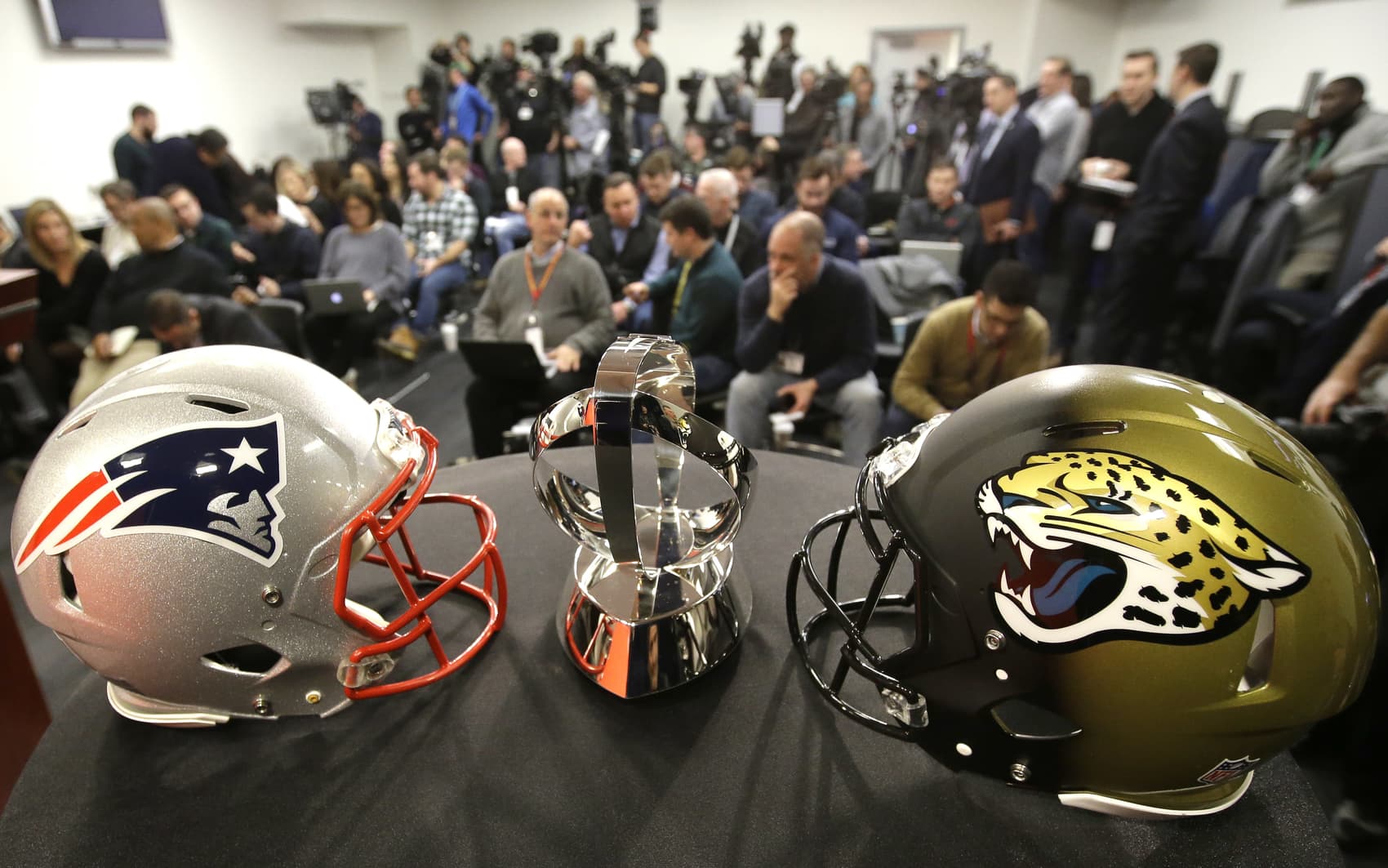 A New England Patriots helmet, left, a Lamar Hunt AFC Championship trophy, center, and a Jacksonville Jaguars helmet, right, are displayed on a podium in front of members of the media, behind, before the start of an NFL football news conference, Wednesday, Jan. 17, 2018, at Gillette Stadium, in Foxborough, Mass. The New England Patriots host the Jacksonville Jaguars in the AFC championship on Sunday (AP Photo/Steven Senne)