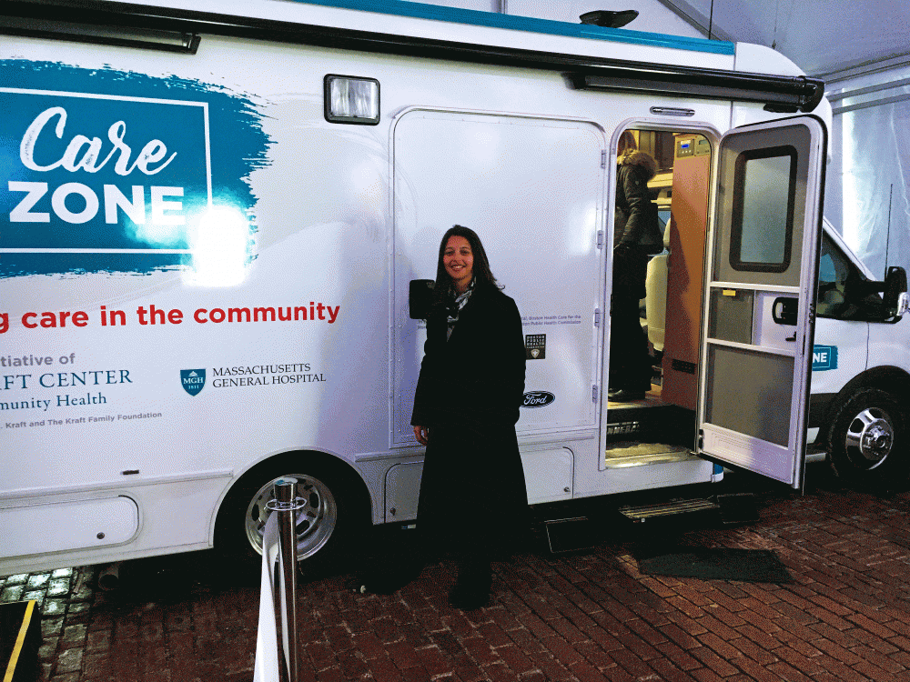 Elsie Taveres, executive director of the Kraft Center for Community Health at MGH, stands in front of the CareZONE mobile van. (Deborah Becker/WBUR)