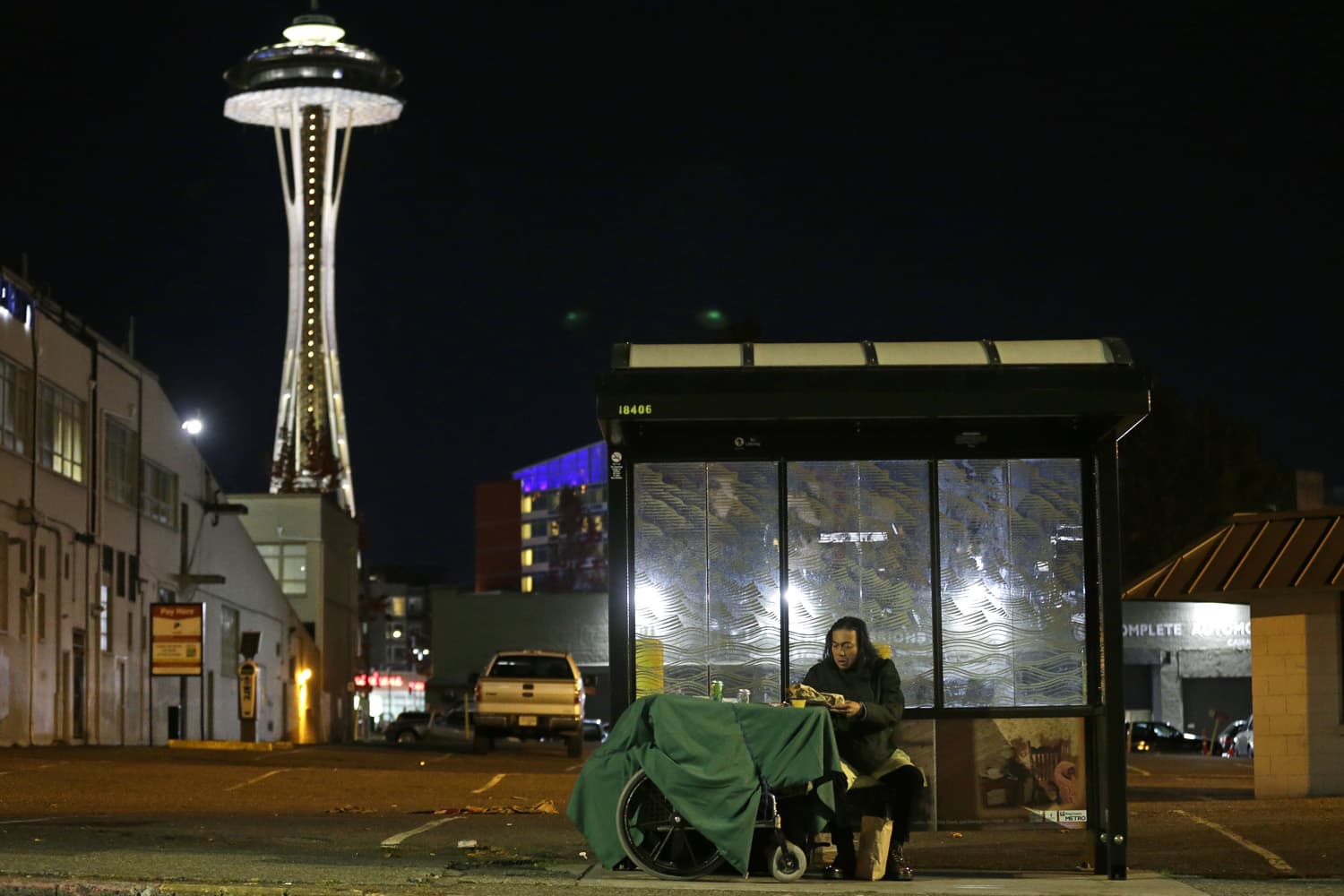 In this Oct. 30, 2017 photo, Dave Chung, who says he has been homeless for five years on the streets of California and Washington state, eats a meal before bedding down in a bus shelter in view of the Space Needle in Seattle. Chung says he has been offered shelter many times, but chooses to remain outside due to the living conditions in homeless shelters and conflicts he has with other people. (AP Photo/Ted S. Warren)