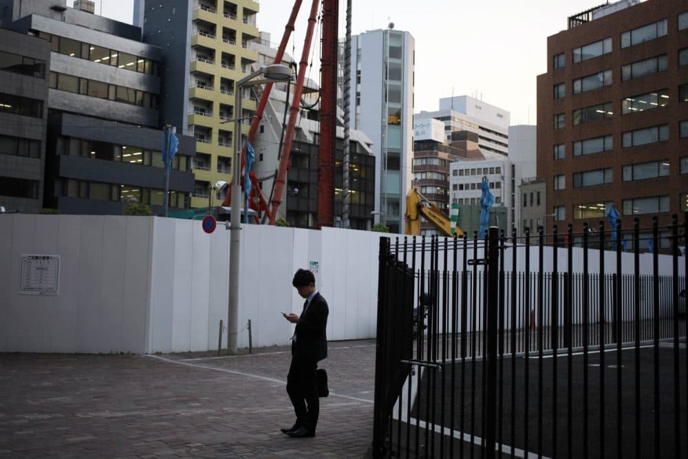 FILE - In this May 8, 2013 file photo, a man looks at his mobile phone near a construction site in Tokyo. (AP Photo/Greg Baker, File)
