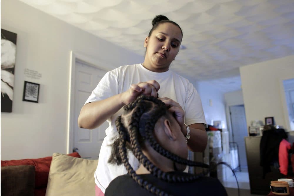 In this Sunday, Feb. 19, 2017 photo Jocelyn DoCouto, top, adds braid extensions for seven-year-old Zanyrah Parrott, of Pawtucket, R.I., in DoCouto's home, in Pawtucket. The billionaire industrialist Charles Koch might not have a lot in common with DoCouto, but they are both part of a national movement to deregulate the business of African-style braiding. DoCouto is pushing for state legislation in Rhode Island that would exempt her from the cumbersome and expensive occupational licensing requirements for hairdressers and barbers. (AP Photo/Steven Senne)