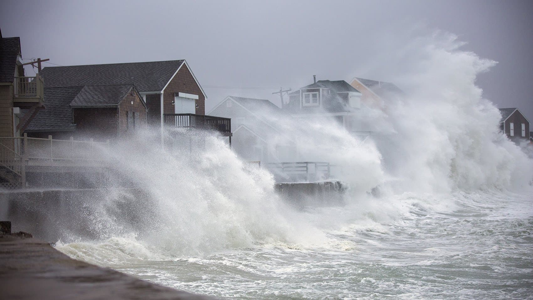 Houses along Lighthouse Road in Scituate are engulfed by waves crashing off the seawall on Friday. (Jesse Costa/WBUR)