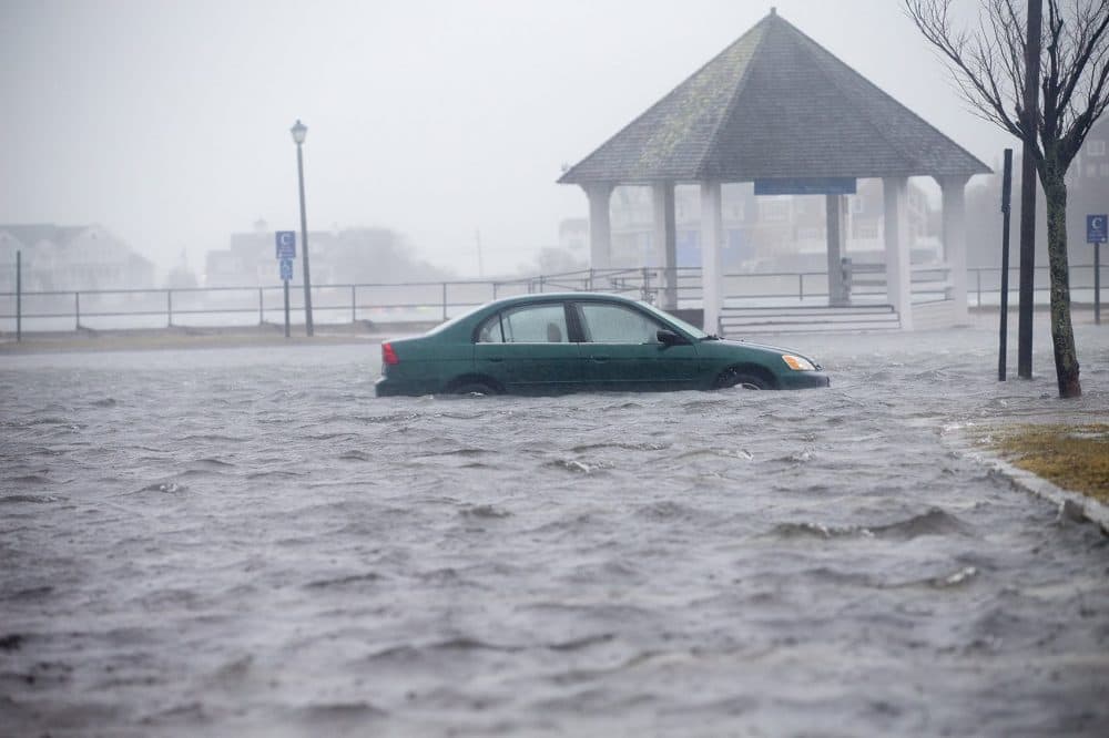 A car sitting in flood water in the parking lot behind the Front St. shops in Scituate. (Jesse Costa/WBUR)