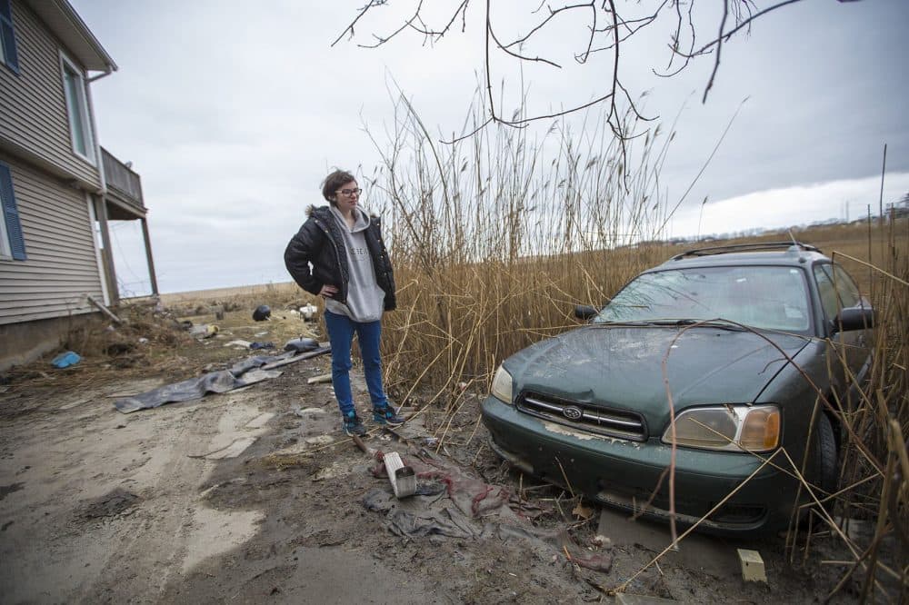 Taylor Fenton stands by one of the family's cars, which was was washed into the marsh by the flood water during the nor'easter Friday. (Jesse Costa/WBUR)
