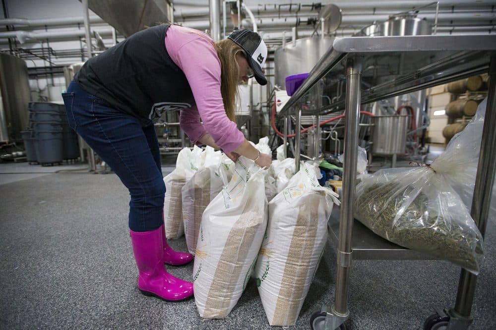 Donning pink boots, Kristen Sykes, founder of the Boston Area Beer Enthusiasts Society (BABES), opens bags of grain to be milled for brewing. (Jesse Costa/WBUR)