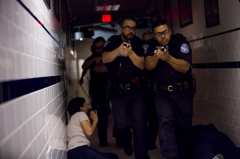 Two CBP officer trainees walk past a woman on the floor as they look to apprehend an active shooter during a drill. (Jesse Costa/WBUR)