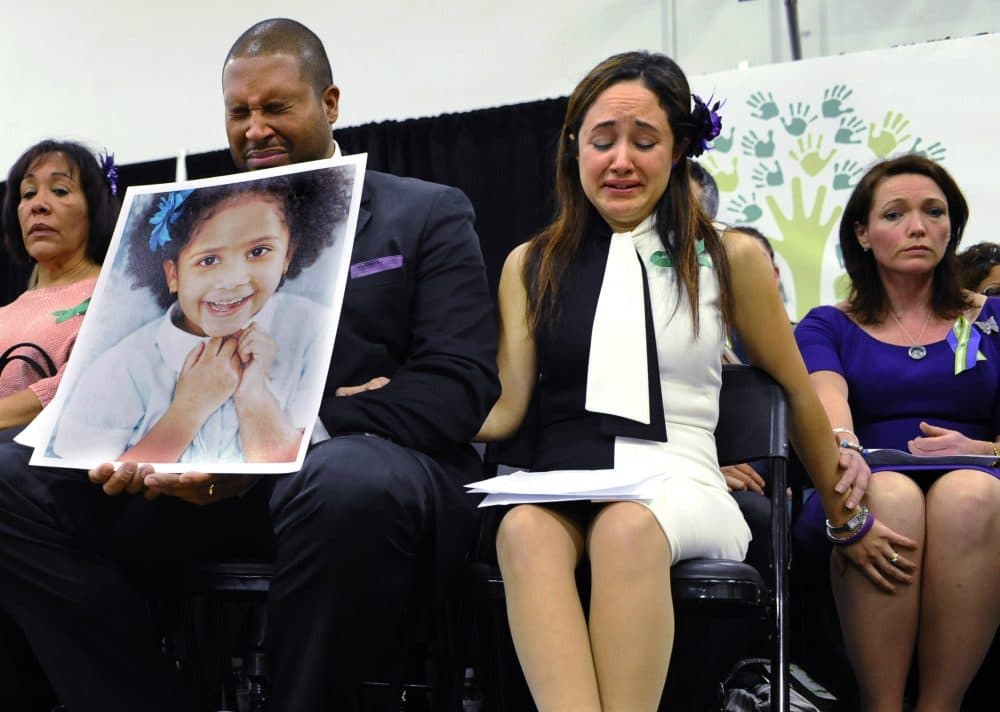In this Jan. 14, 2014 file photo, Jimmy Greene, foreground left, Nelba Marquez-Greene, center, parents of Sandy Hook Elementary School shooting victim Ana Marquez-Greene, shown in the large photograph, and Nicole Hockley, right, mother of victim Dylan Hockley, react during a news conference at Edmond Town Hall in Newtown, Conn. (Jessica Hill/AP)