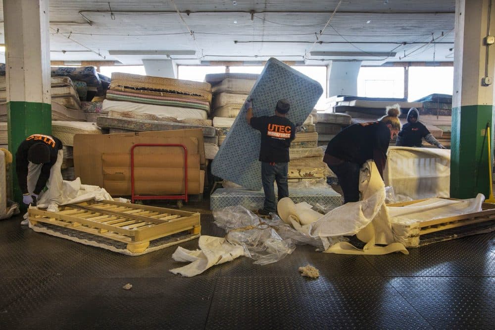 Workers at the UTEC Mattress Warehouse tackle piles of mattresses to breakdown for landfills. (Jesse Costa/WBUR)