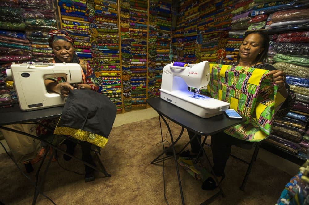 Ebby Ihionu (right) and her sister Ifeyinwa Okolie work on clothing pieces made with African fabrics at Elegance African Fashions in Dorchester. (Jesse Costa/WBUR)