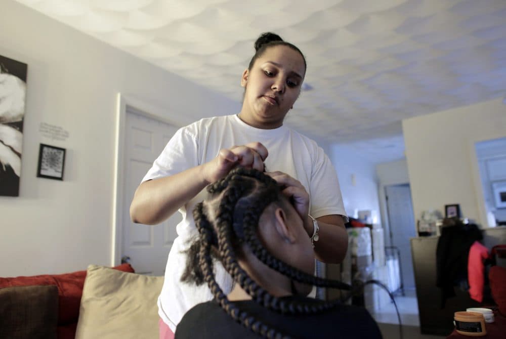 In this Sunday, Feb. 19, 2017 photo Jocelyn DoCouto, top, adds braid extensions for 7-year-old Zanyrah Parrott, of Pawtucket, R.I., in DoCouto's home, in Pawtucket. DoCouto is pushing for state legislation in Rhode Island that would exempt her from the cumbersome and expensive occupational licensing requirements for hairdressers and barbers. (Steven Senne/AP)