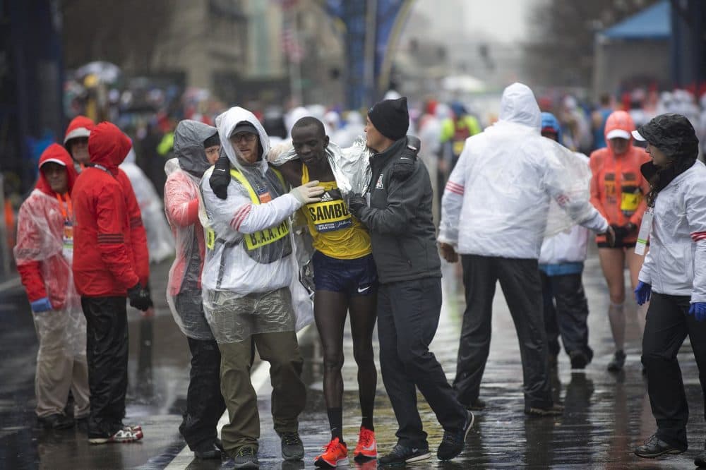 Marathon officials assist Stephen Sambu toward the medical tent. (Jesse Costa/WBUR)