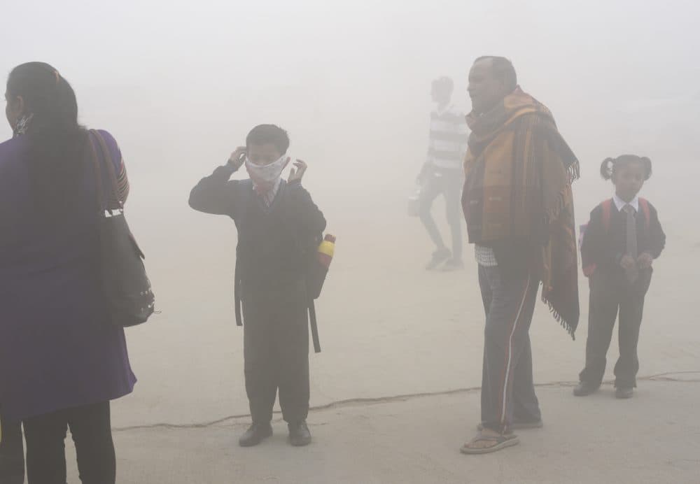 In this Nov. 9, 2017 photo, an Indian boy uses a handkerchief to protect his face as school children and parents await transport surrounded by morning smog on the outskirts of New Delhi, India. (R S Iyer/AP)